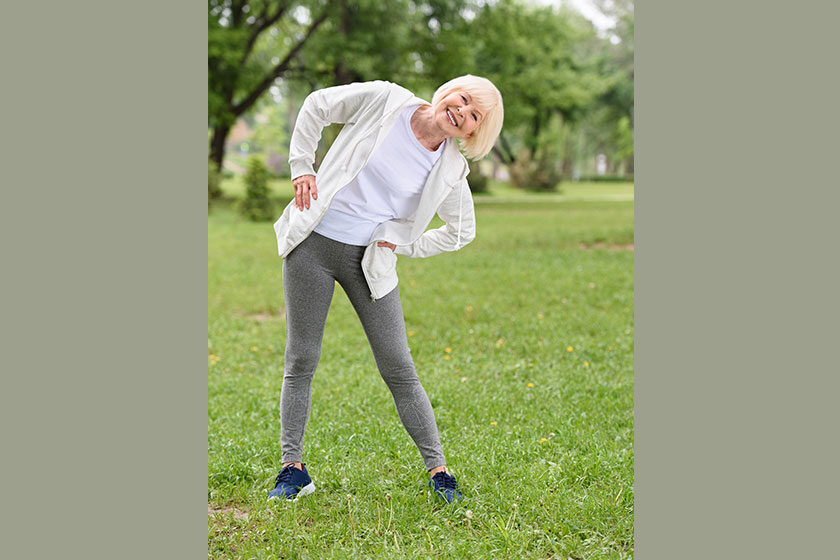 Happy senior sportswoman exercising on green lawn in park