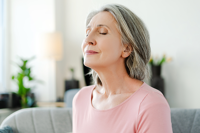 Smiling active senior woman sitting with closed eyes on comfortable sofa relaxing at home. Happy female, freelancer taking a break, resting. Natural beauty, healthy lifestyle concept 