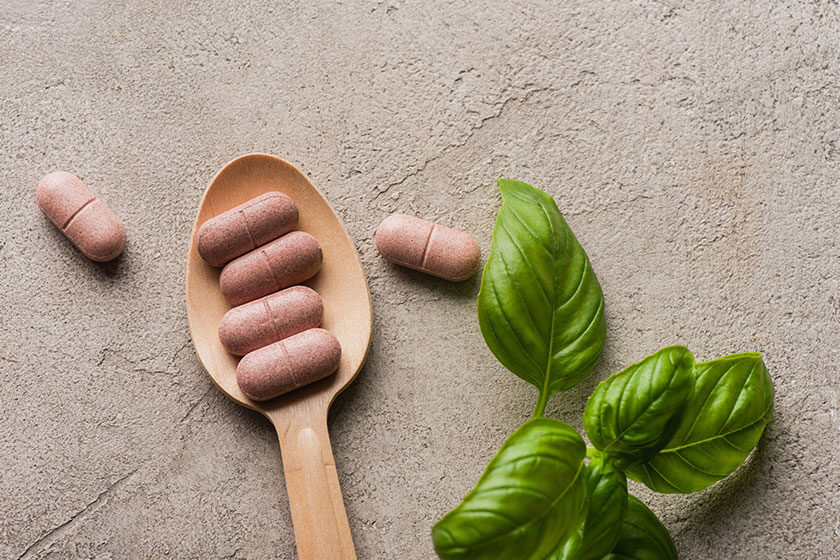 Top view of green leaves and pills in wooden spoon on concrete background, naturopathy concept